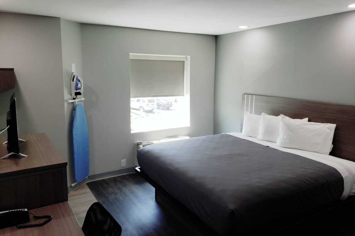 A modern hotel room with a large bed, a desk with a computer, and a window with a view of parked cars.
