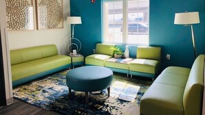 A room with teal walls, a green sofa, a blue ottoman, and a window with a view of parked cars. - Hathaway Inn (Panama City)