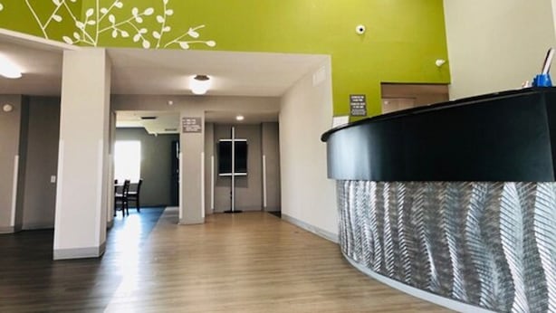 A reception area with a curved black counter, a green accent wall, and a wooden floor. - Hathaway Inn (Panama City)