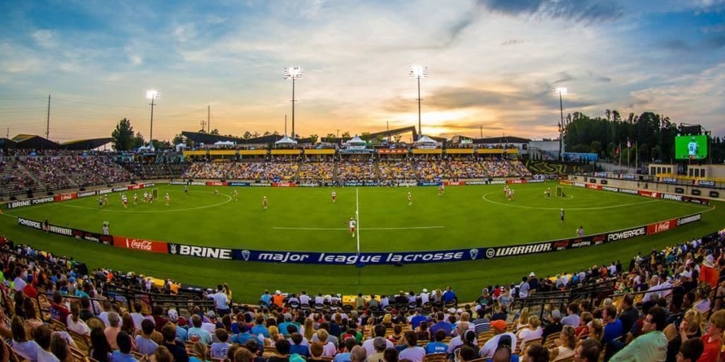 A stadium with multiple tiers of seating, a soccer field, and advertisements for major league lacrosse.