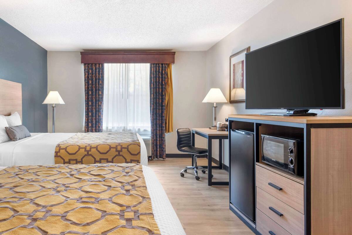 Une chambre d’hôtel équipée d’un lit, d’un bureau, d’une télévision, d’un four à micro-ondes et d’une fenêtre avec des rideaux.