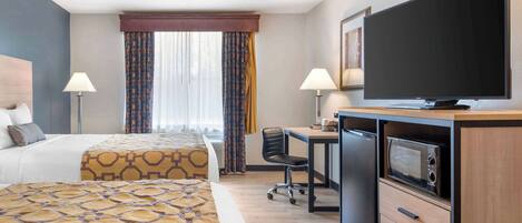 A hotel room with a bed, desk, television, microwave, and a window with curtains.