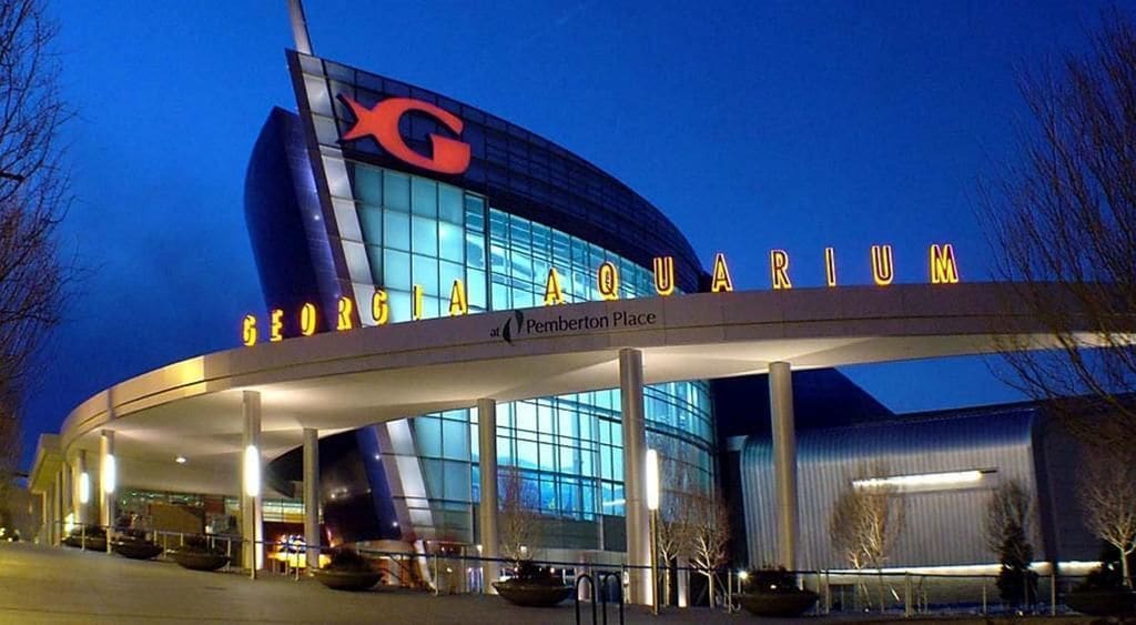 The exterior of the Georgia Aquarium with a large 'C' logo, a curved glass facade, and the name 'Pemberton Place' beneath.