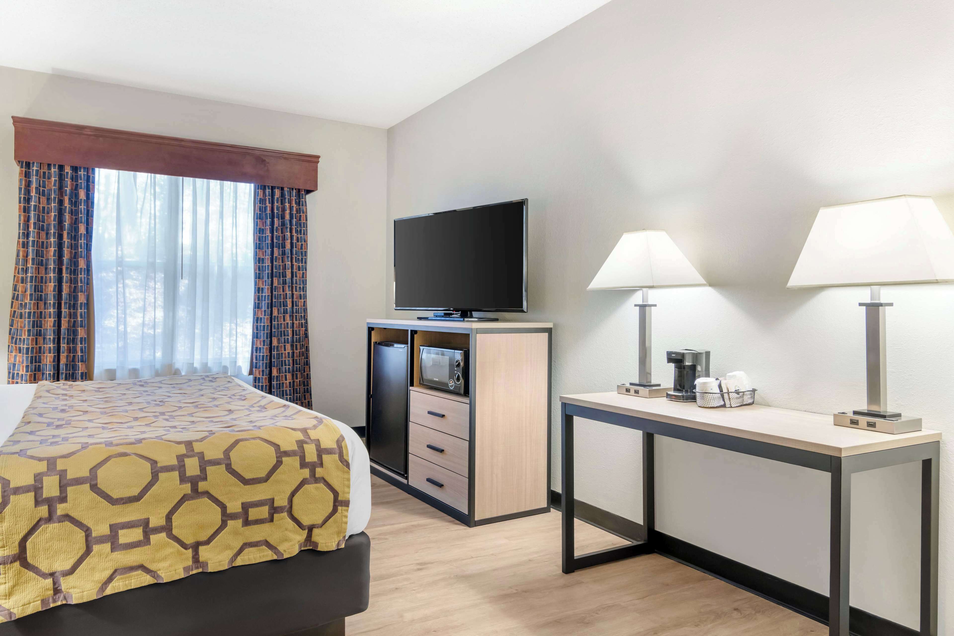 A hotel room with a bed, a desk with a television, two lamps, and a coffee maker.