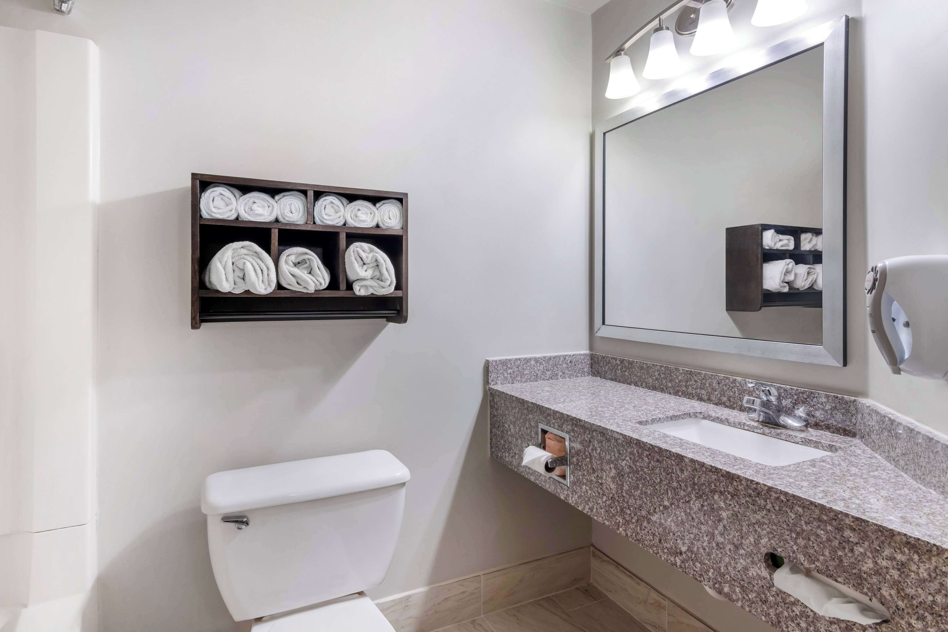 A modern bathroom with a white toilet, a granite countertop sink, a large mirror, and a towel rack with neatly folded towels.