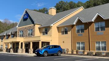 A hotel with a stone facade, multiple windows, and a blue car parked in front.