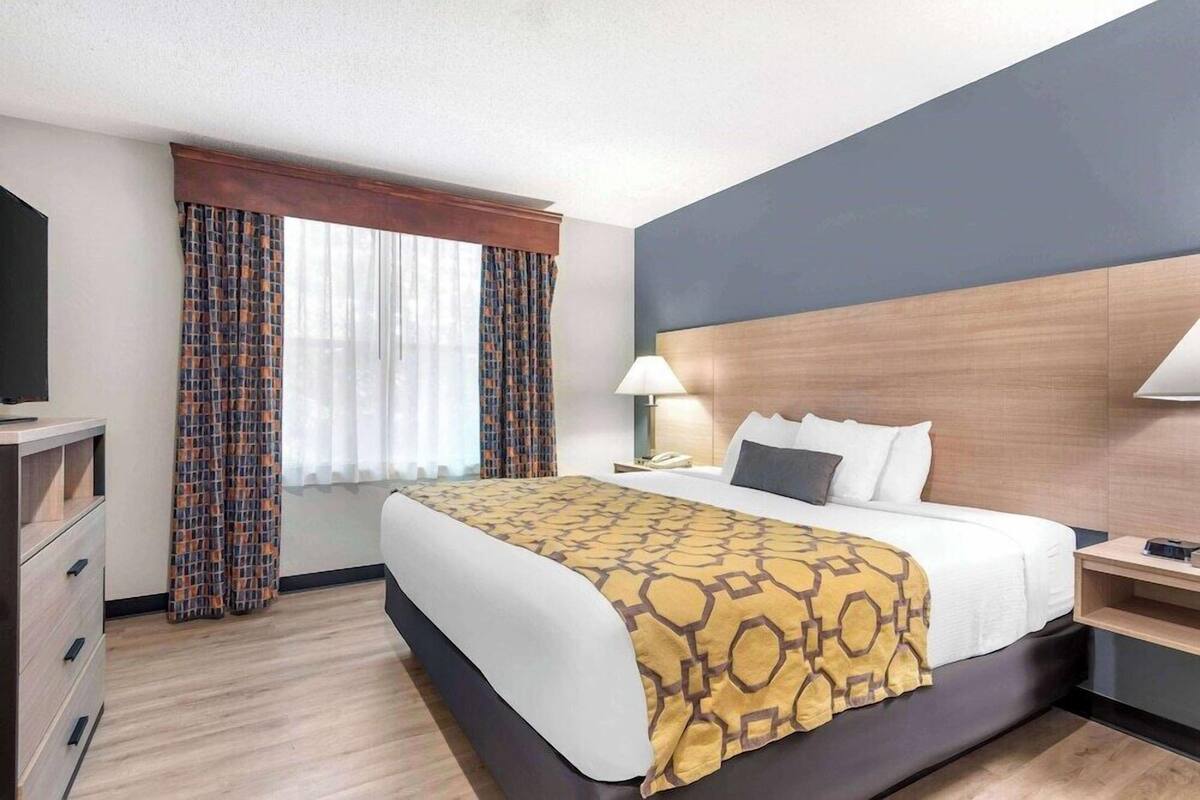 Une chambre d’hôtel avec un lit, un bureau, une chaise, une télévision et une fenêtre avec des rideaux.