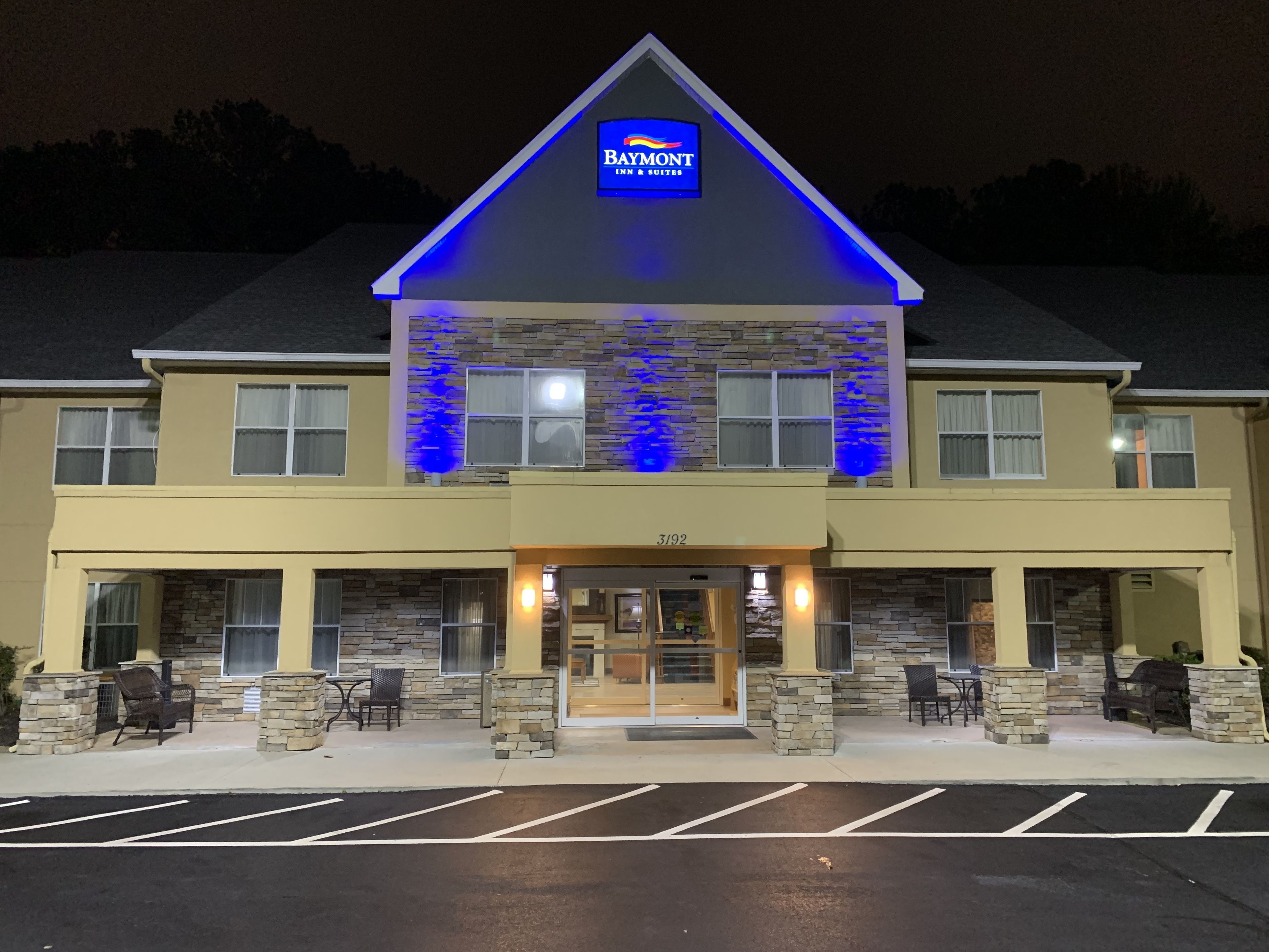 A Baymont Inn & Suites building with a stone facade, a blue-lit entrance, and a parking lot.