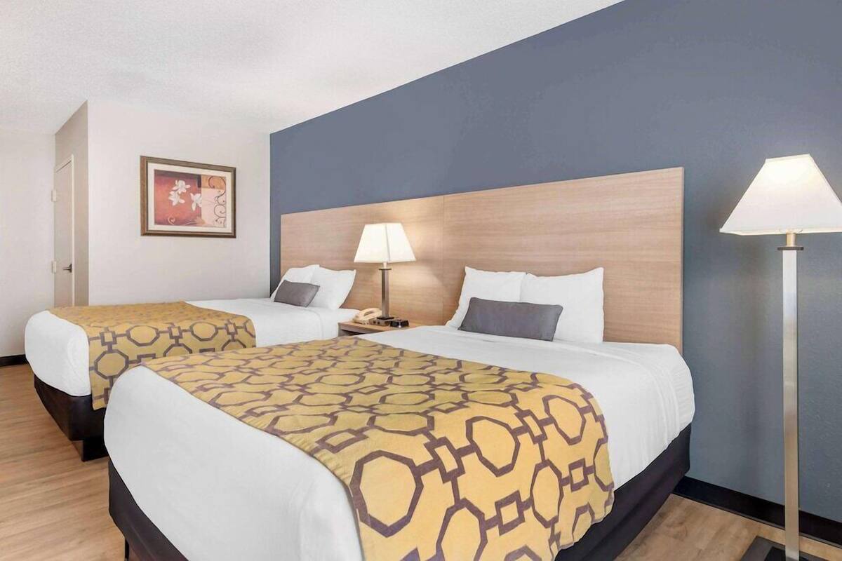 Une chambre d’hôtel avec deux lits, une tête de lit en bois, des lampes de chevet, un tableau encadré au mur et un lampadaire.