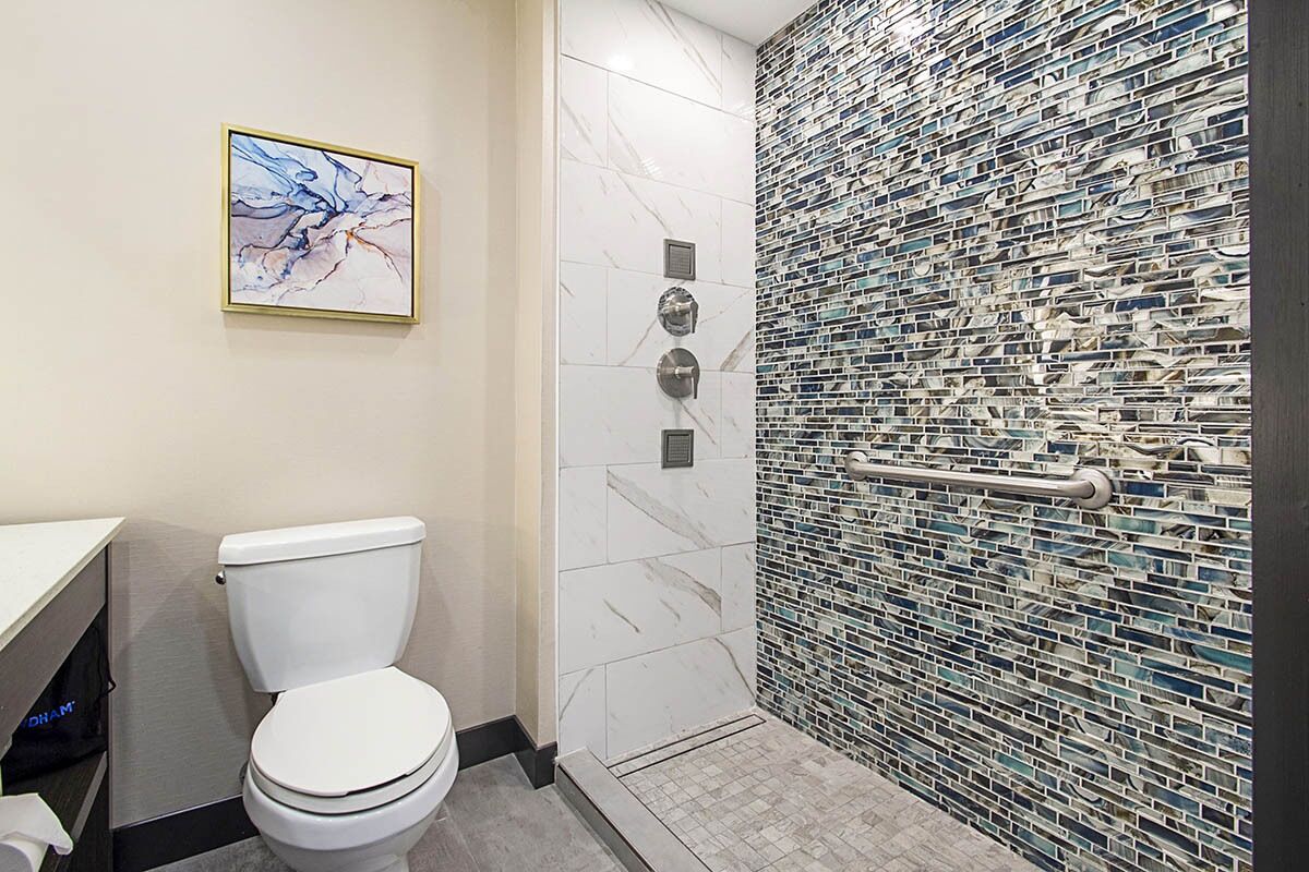 A modern bathroom with a white toilet, a shower with a mosaic tile wall, and a framed abstract painting on the wall.