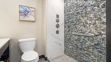 A modern bathroom with a white toilet, a shower with a mosaic tile wall, and a framed abstract painting on the wall.