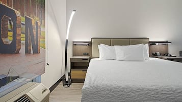 Une chambre d’hôtel avec un grand lit, une table de chevet, une lampe et un climatiseur fixé au mur.