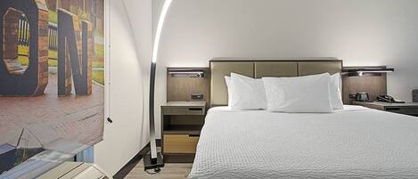 A hotel room with a large bed, a nightstand, a lamp, and a wall-mounted air conditioner.