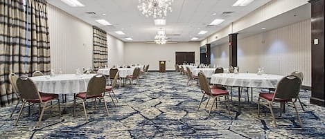 A conference room with multiple round tables, chairs, and a carpeted floor.