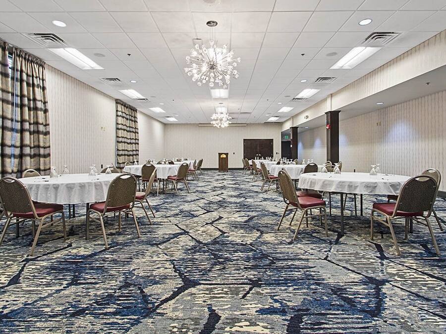 A conference room with multiple round tables, chairs, and a carpeted floor.