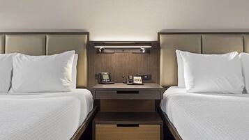 Une chambre d’hôtel avec deux lits, une table de chevet avec un téléphone et une petite table, ainsi qu’un tiroir sous le lit.