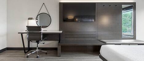 A modern bedroom with a bed, a desk, a chair, a large mirror, and a window.