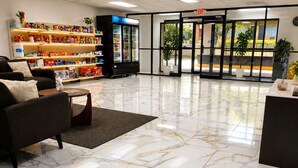 A hotel lobby with a marble floor, a sofa, a coffee table, a refrigerator, and shelves with snacks. - Heritage Inn Cartersville (Cartersville)
