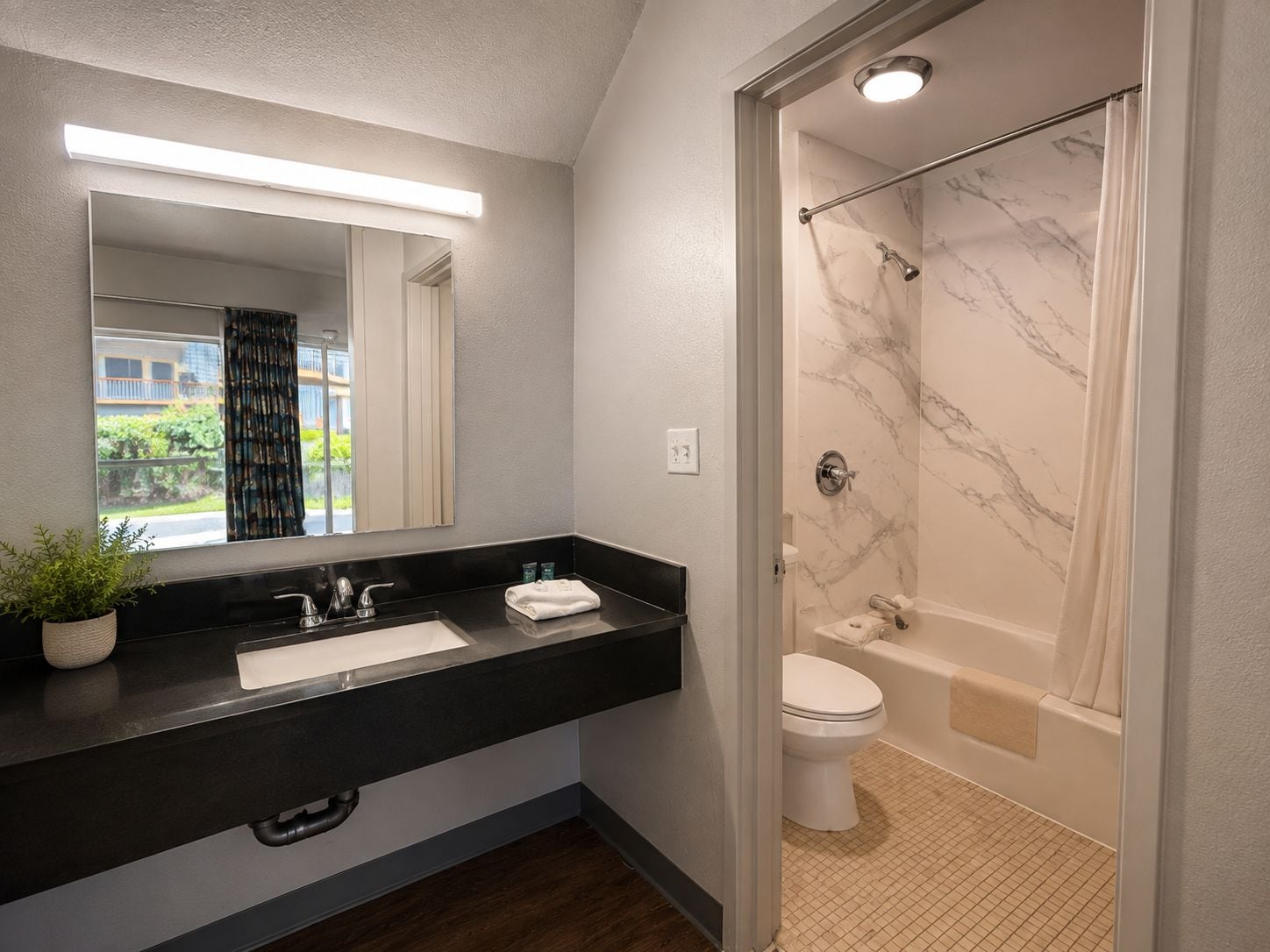 A modern bathroom with a black countertop, a white sink, a mirror, a shower with marble walls, and a toilet.