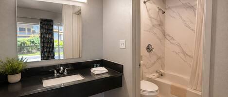 A modern bathroom with a black countertop, a white sink, a mirror, a shower with marble walls, and a toilet.