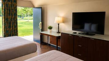 Une chambre d’hôtel avec un lit, un bureau avec une télévision et une vue sur un espace extérieur verdoyant.