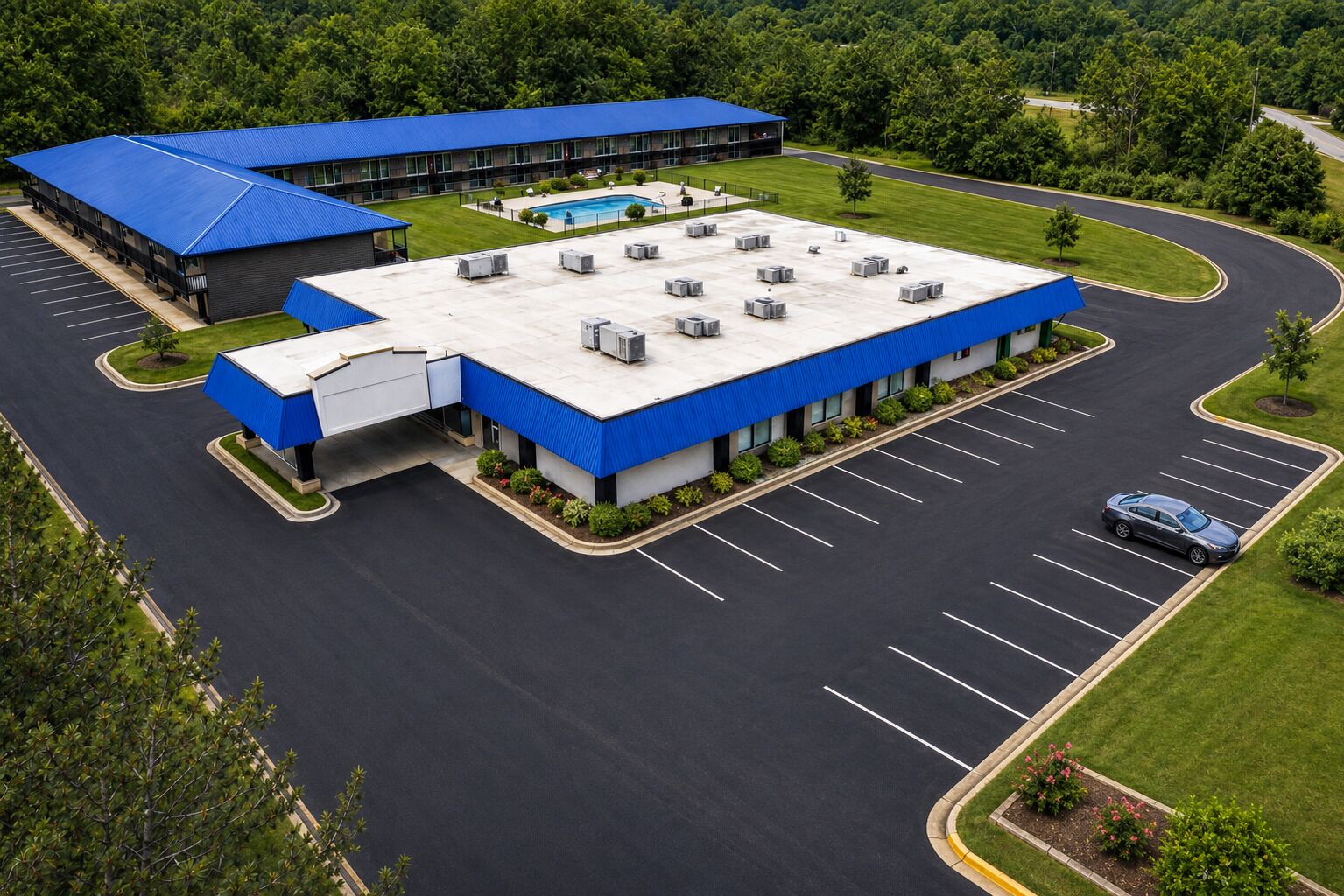 A large building with a blue roof, a swimming pool, and a parking lot with a car.