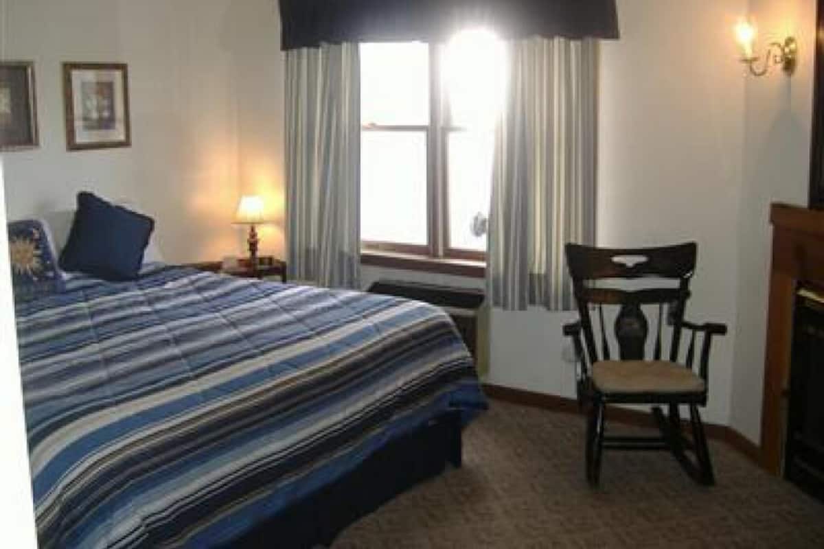 Une chambre à coucher comprenant un lit, une chaise, une fenêtre avec des rideaux, une lampe et des appliques murales.