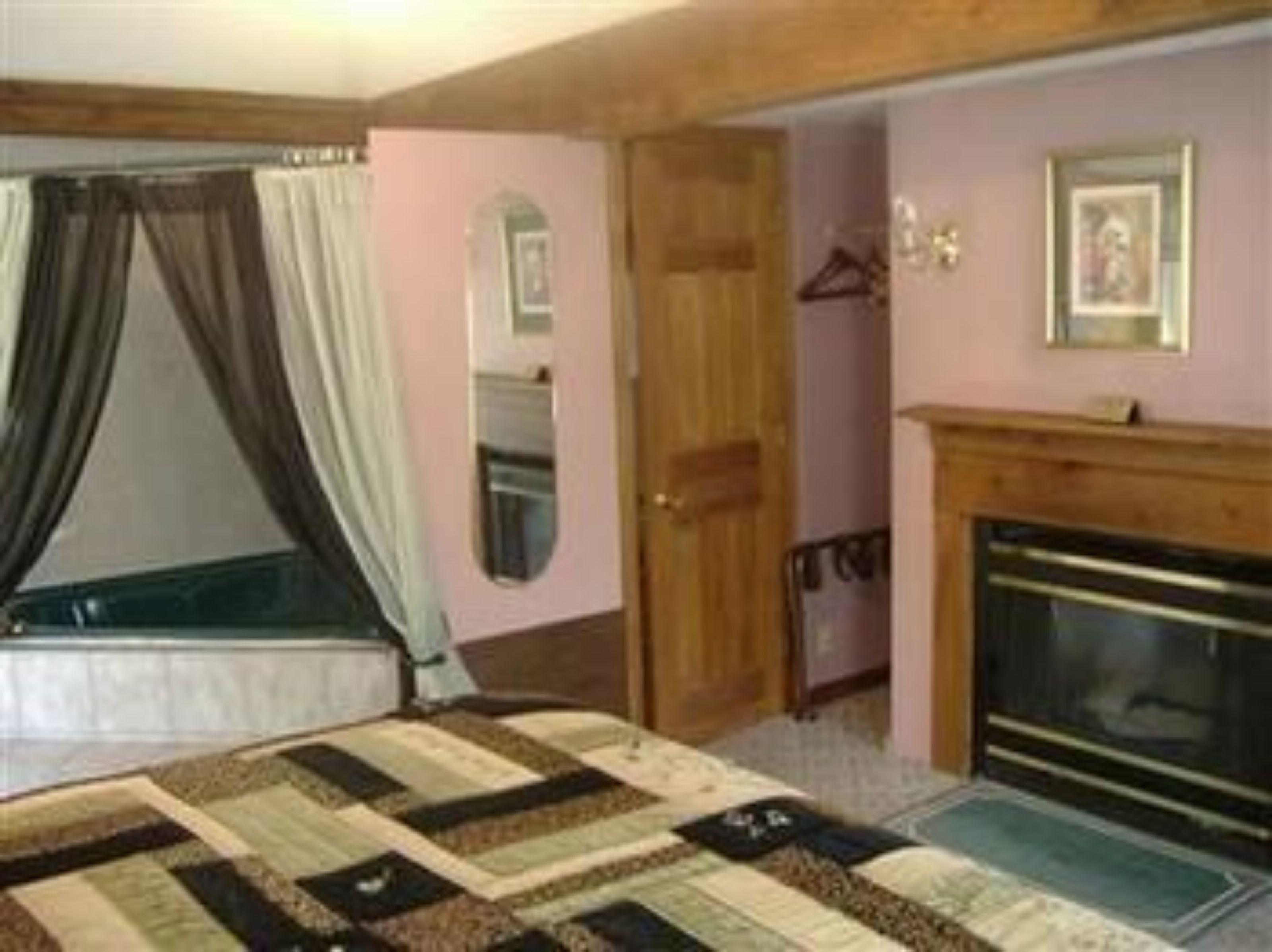 Un dormitorio con cama, puerta de madera, espejo, chimenea y perchero.