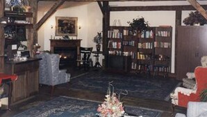 A rustic room with exposed wooden beams, a fireplace, a bookshelf, and a chandelier. - Sturbridge Country Inn (Fiskdale)