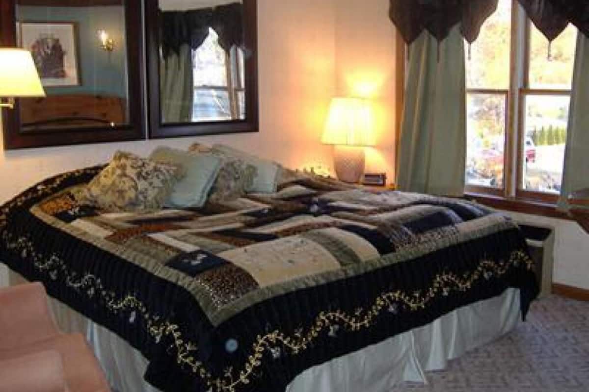 Une chambre à coucher avec un grand lit, une lampe de chevet, un miroir et une fenêtre avec des rideaux.