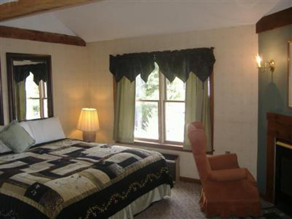 Un dormitorio con una cama grande, una silla, una ventana con cortinas y una lámpara.