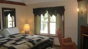 Un dormitorio con una cama grande, una silla, una ventana con cortinas y una lámpara.