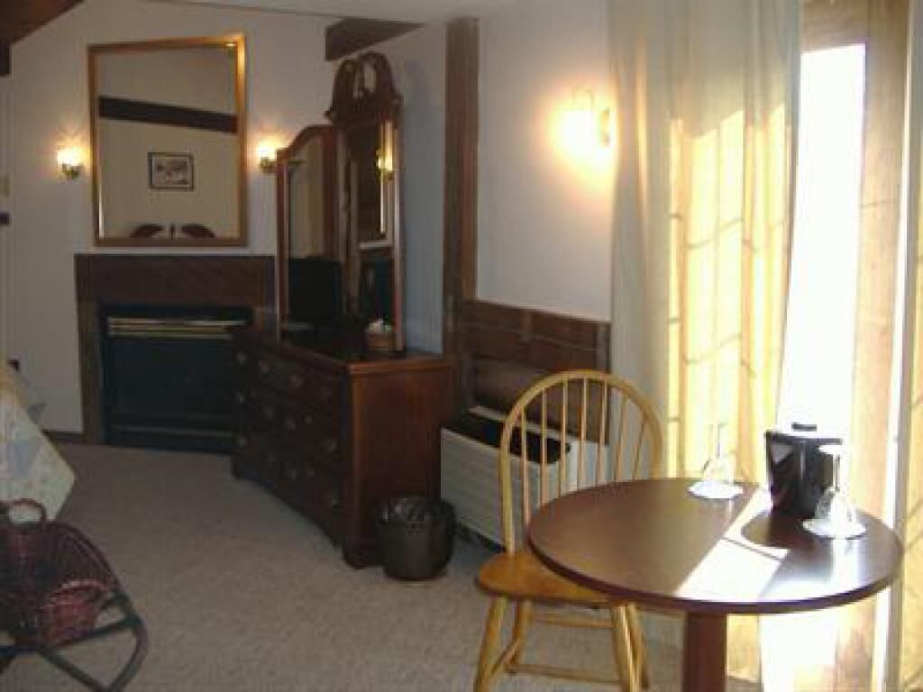 A room with a wooden table, a chair, a dresser, a mirror, and a window with curtains.