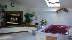 A room with a fireplace, a large window, and a jacuzzi tub. - Sturbridge Country Inn (Fiskdale)