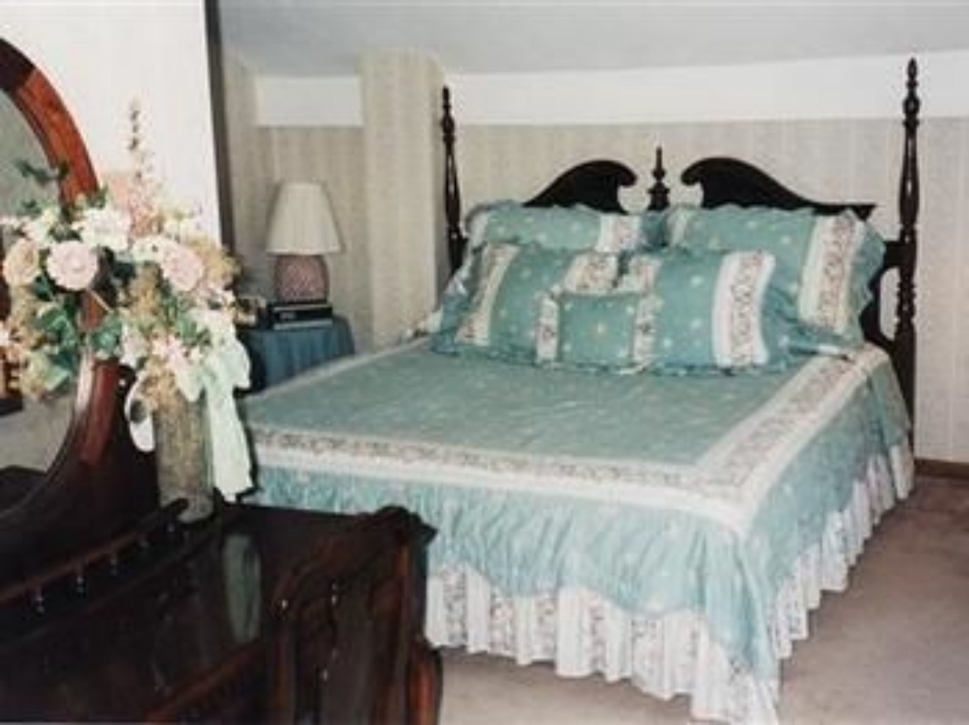 A bedroom with a four-poster bed, a wooden dresser, and a vase of flowers.