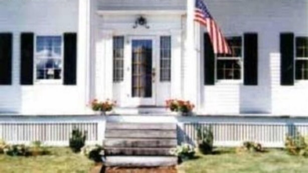 A white two-story building with a central entrance, columns, and an American flag. - Sturbridge Country Inn (Fiskdale)