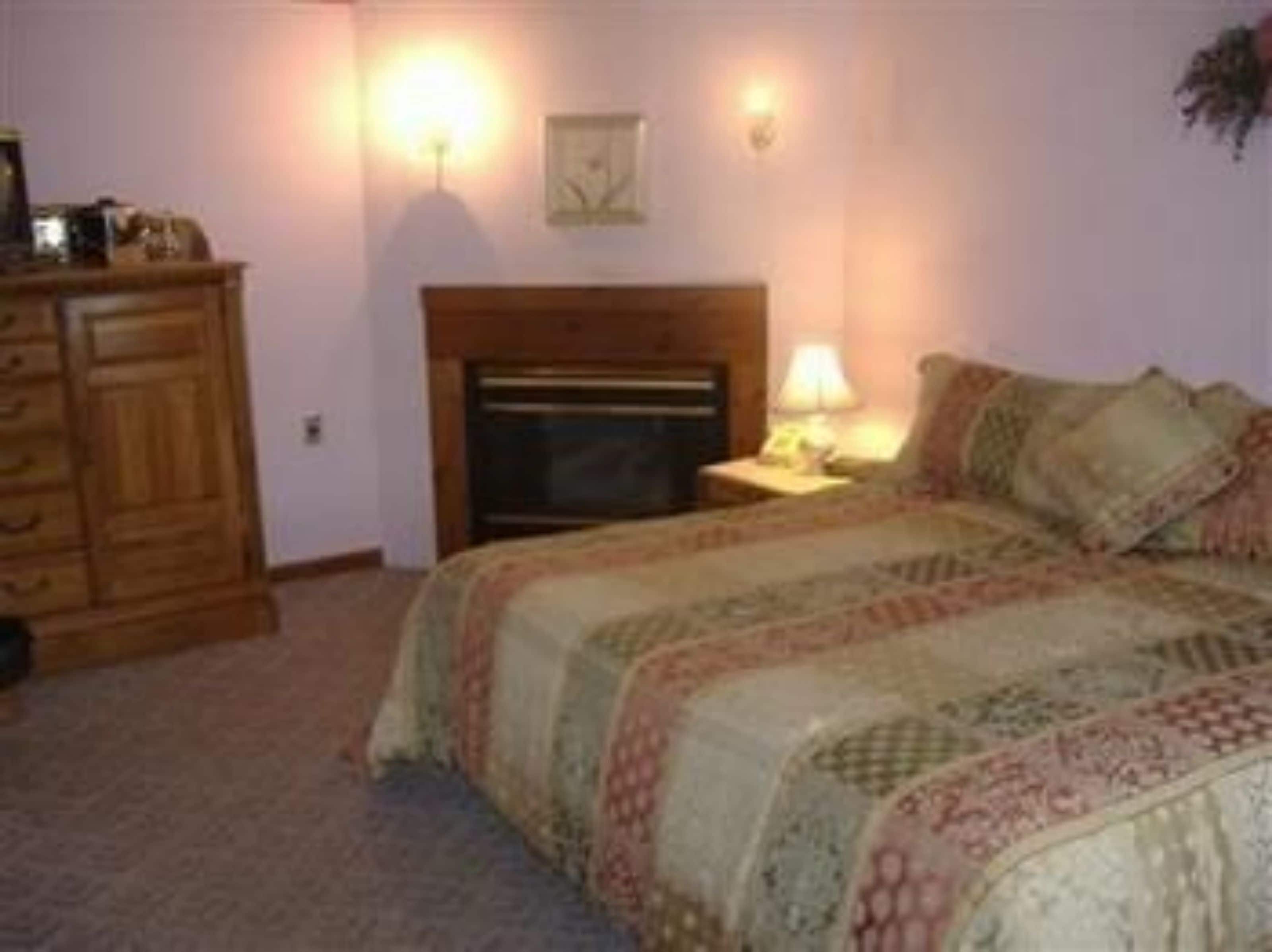 A bedroom with a bed, dresser, nightstand, lamp, and a fireplace.