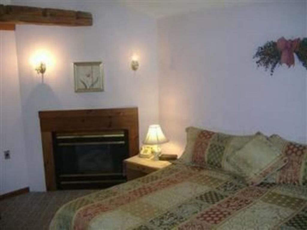 Un dormitorio con cama, mesita de noche, lámpara, chimenea e iluminación en la pared.