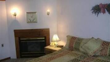Un dormitorio con cama, mesita de noche, lámpara, chimenea e iluminación en la pared.