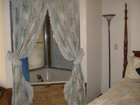 A bedroom with a bed, a window with curtains, a floor lamp, and a wooden chair.