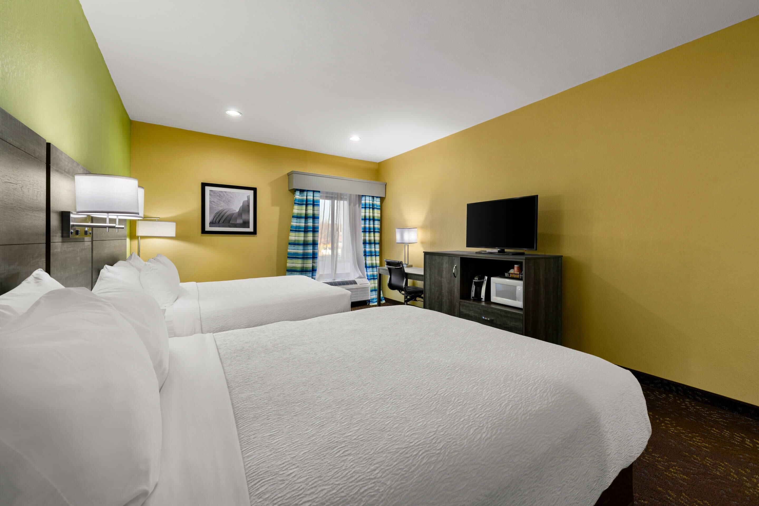 A hotel room with two beds, a desk, a television, and a window with curtains.