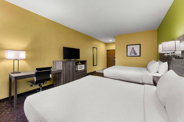 Habitación de hotel con una cama grande, un escritorio con silla, un televisor y un microondas.