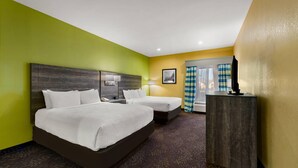 A hotel room with two beds, a desk, a lamp, and a view of the outdoors.