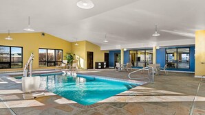 An indoor swimming pool with clear water, surrounded by stone tiles, and equipped with poolside chairs and a sunshade.