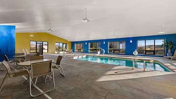 An indoor swimming pool area with hexagonal tiles, seating, and large windows.