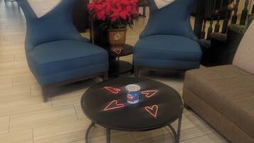 Una zona de estar con dos sillones azules, una mesa redonda con palomitas y adornos con forma de corazón, y una planta en maceta.
