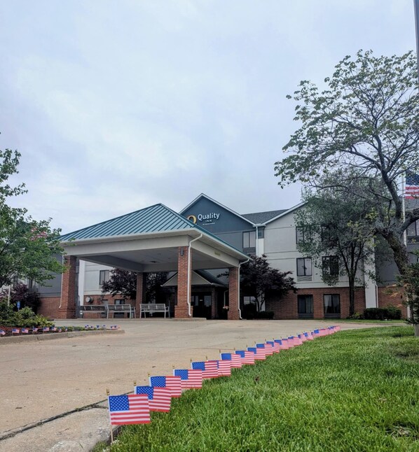 Um hotel Quality Inn com entrada coberta, decoração com a bandeira americana e área gramada na frente.