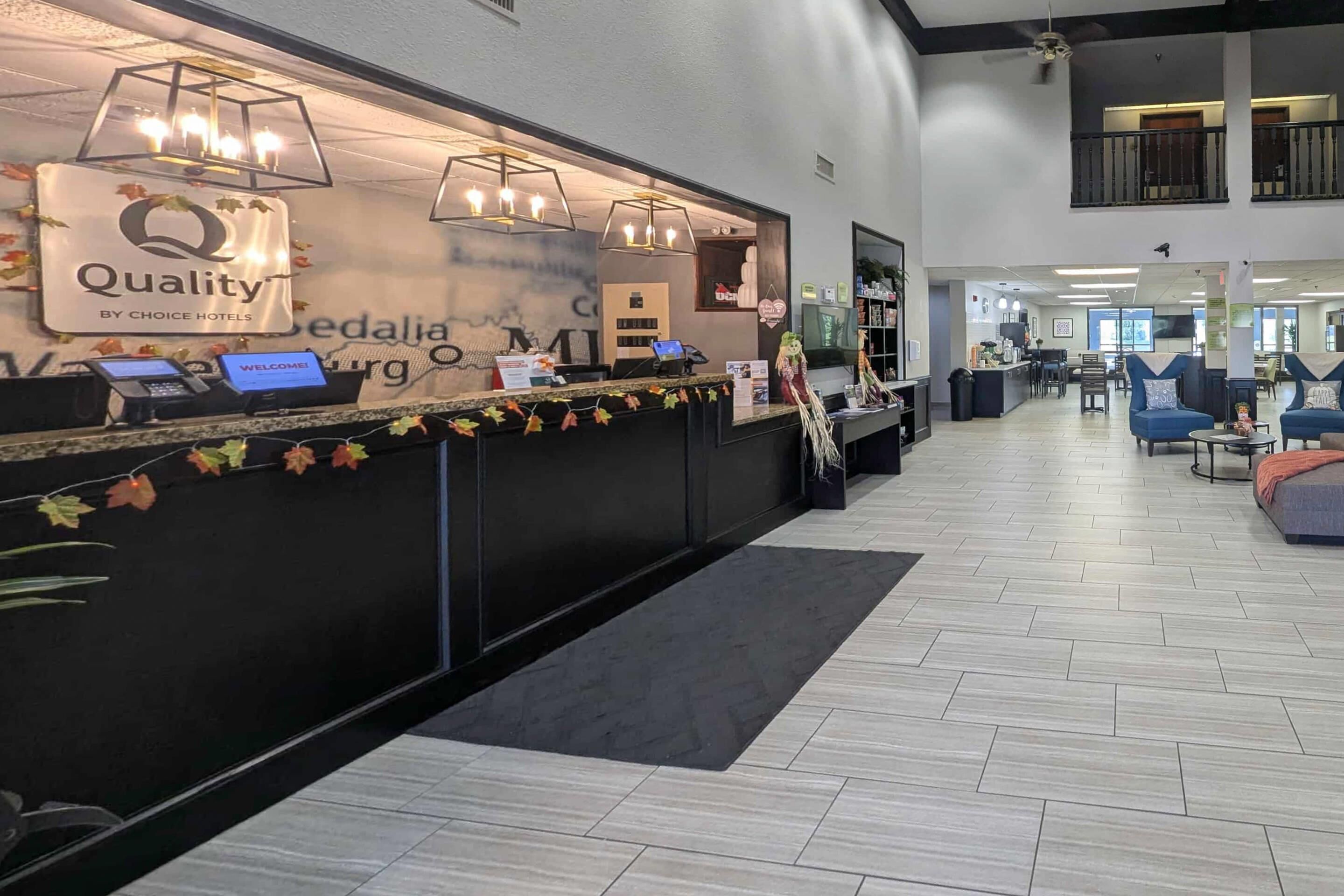 A hotel reception area with a modern design, including a reception desk, a digital screen, and a sign indicating the hotel name.