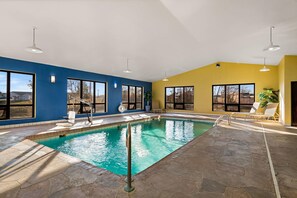 Uma piscina interior com água azul cristalina, rodeada por grandes janelas e um chão de pedra.