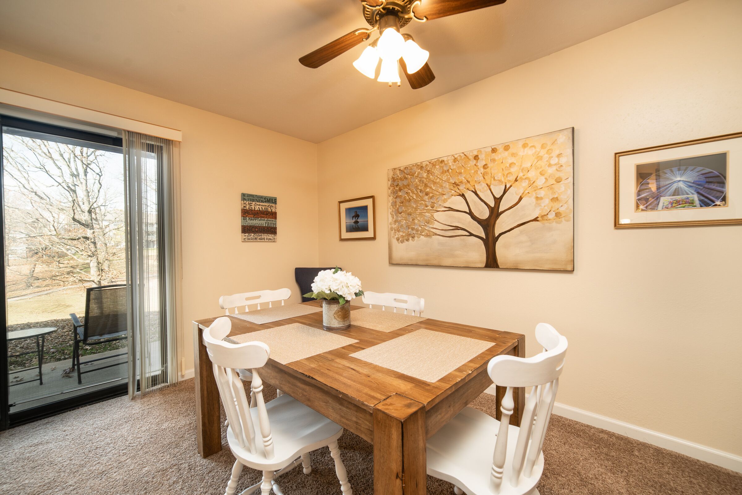 A dining area with a wooden table, white chairs, and a ceiling fan.